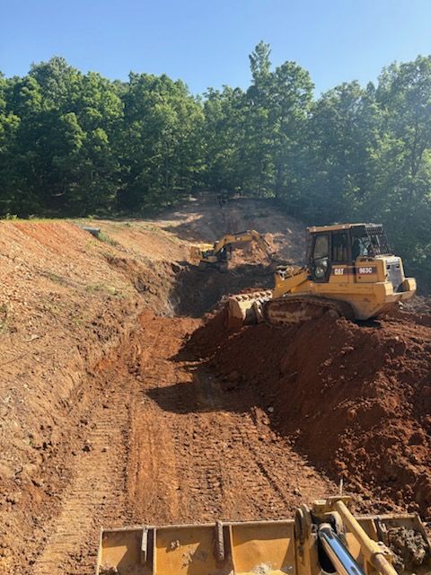 Bulldozer grading a red dirt excavation site under green trees