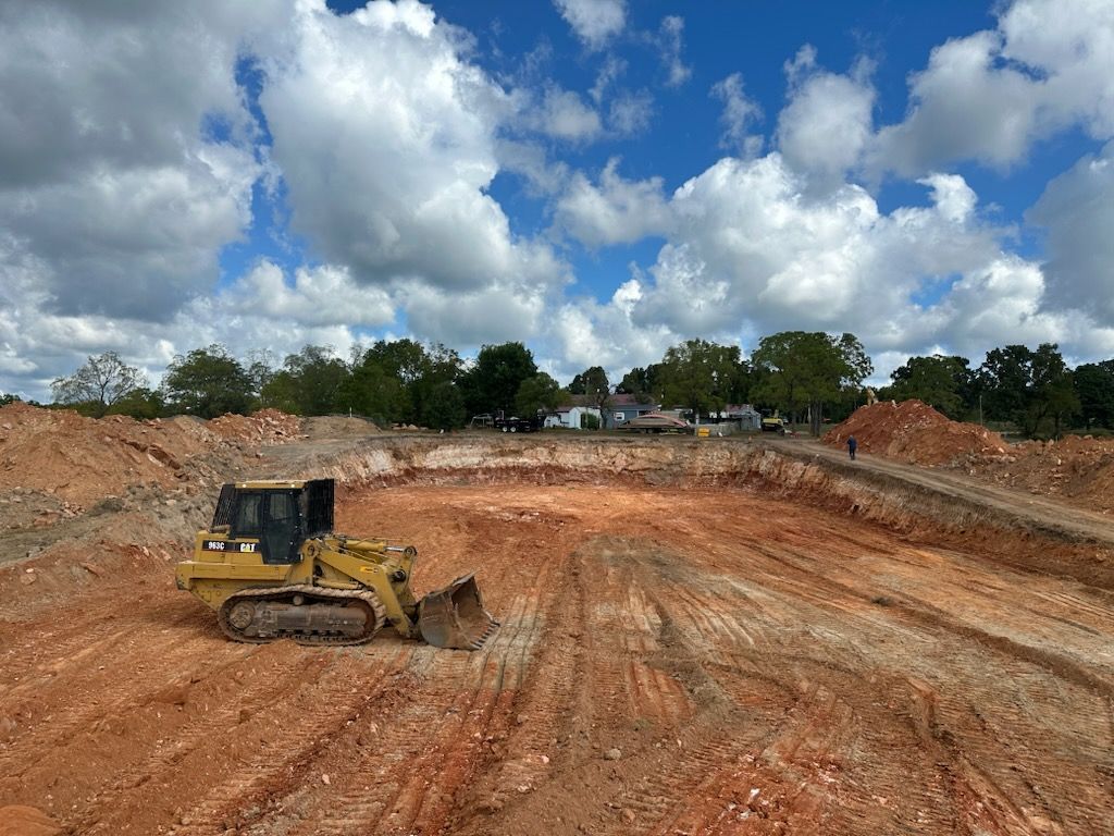 Yellow bulldozer grading a red dirt construction site under a cloudy sky