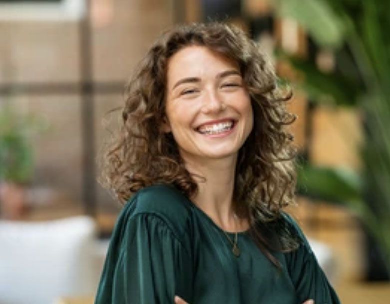 A woman with curly hair is smiling with her arms crossed.