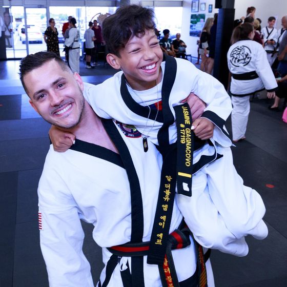 a man is carrying a young boy who is wearing a black belt that says ' yasmine daimaowo ' on it
