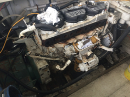 A disassembled marine engine sits in a boat compartment, featuring black valve covers and various hoses and components.