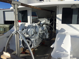 A large white marine engine sits on blocks on the back deck of a white boat, supported by a metal frame.