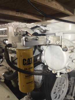 A yellow Caterpillar fuel filter attached to a white engine component with a custom metal mounting bracket.