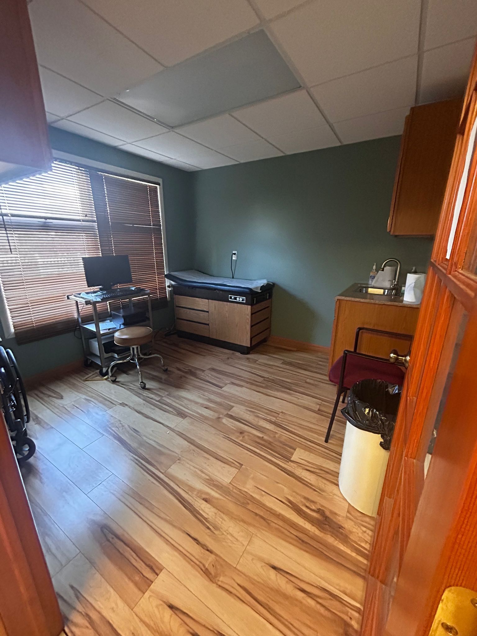 A room with hardwood floors , a desk , a computer and a trash can.