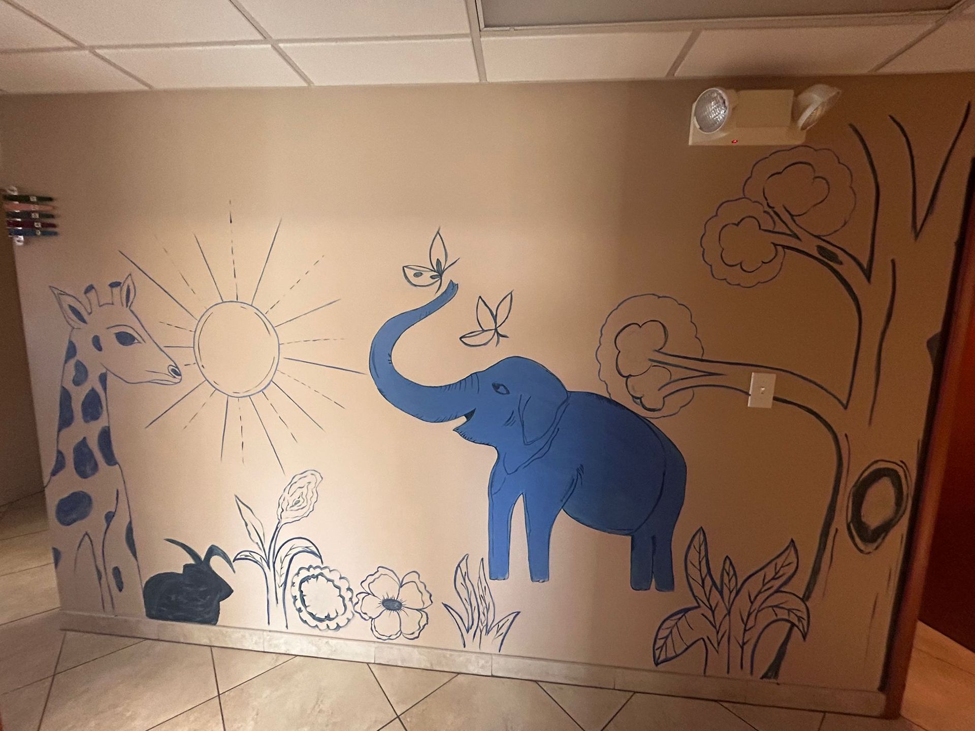 A blue elephant is painted on a wall next to a giraffe.