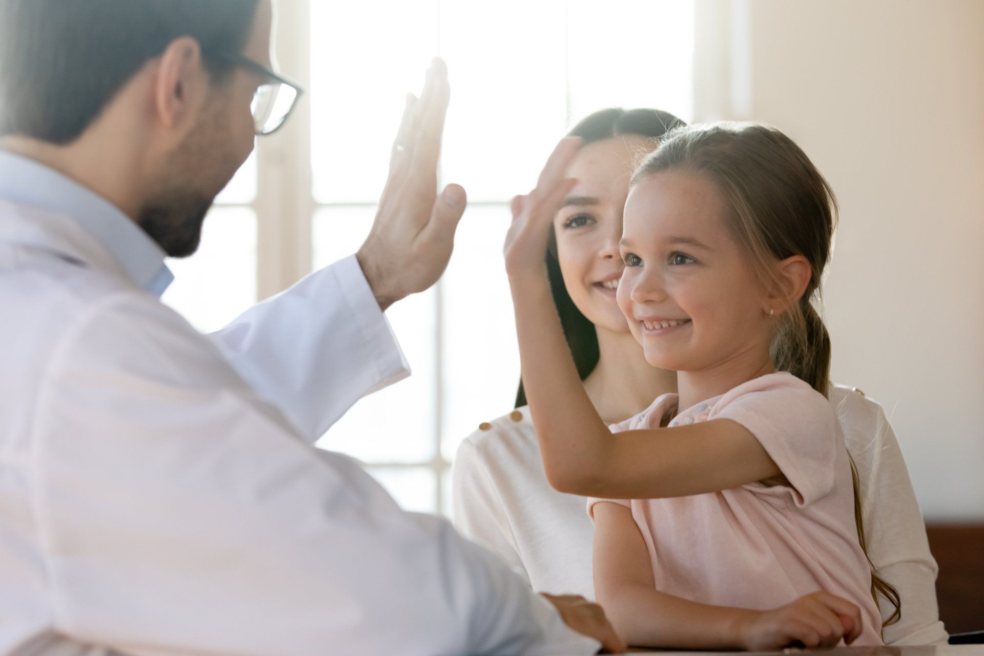 A child sitting in her mother's lap give a pediatrician a high five