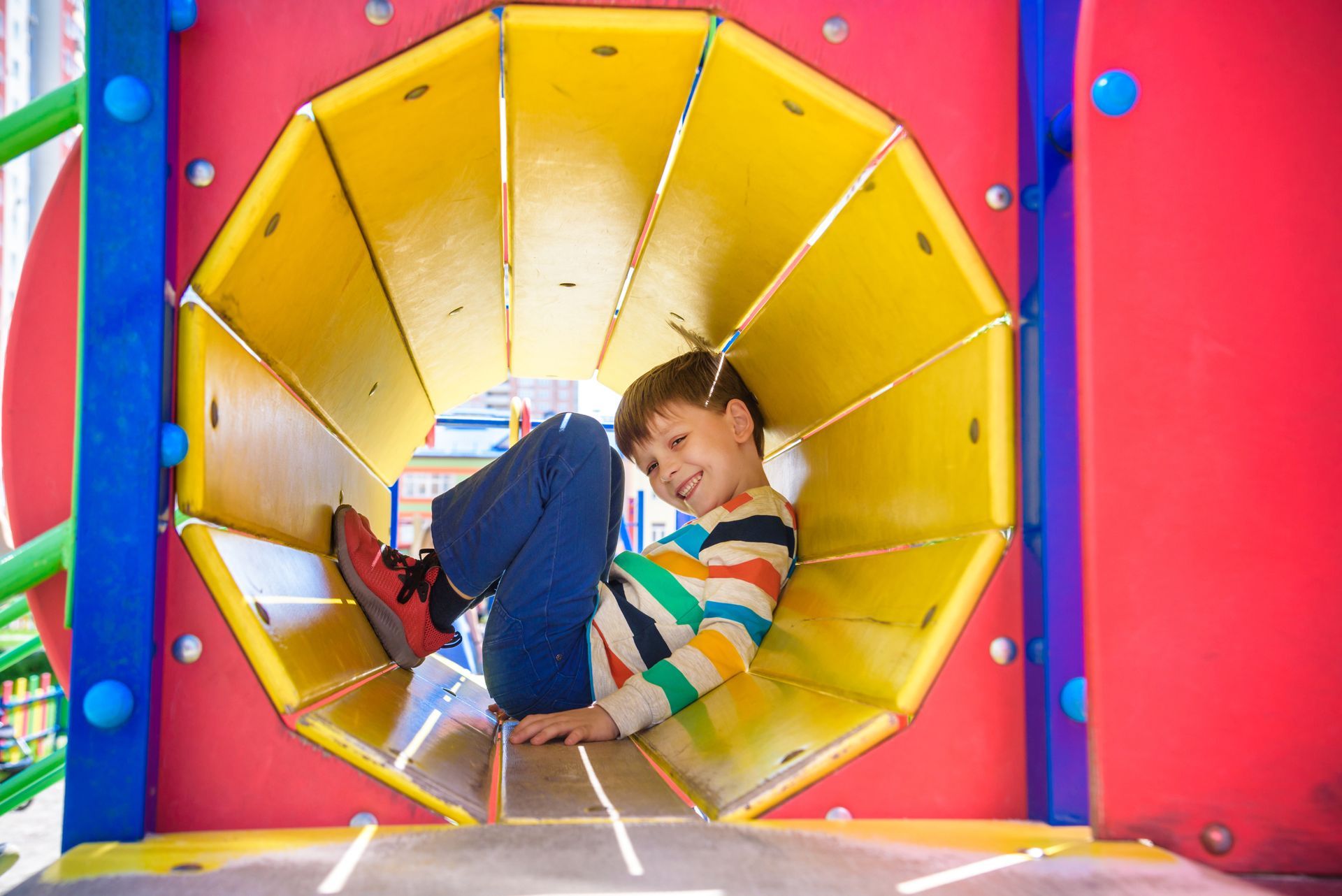 Boy smiles while inside a colorful playground tunnel.