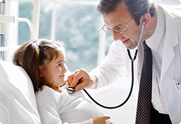 A doctor is listening to a little girl 's heartbeat with a stethoscope.