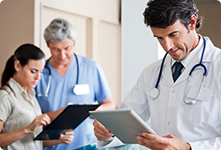 A doctor is looking at a tablet while two nurses look at a clipboard.