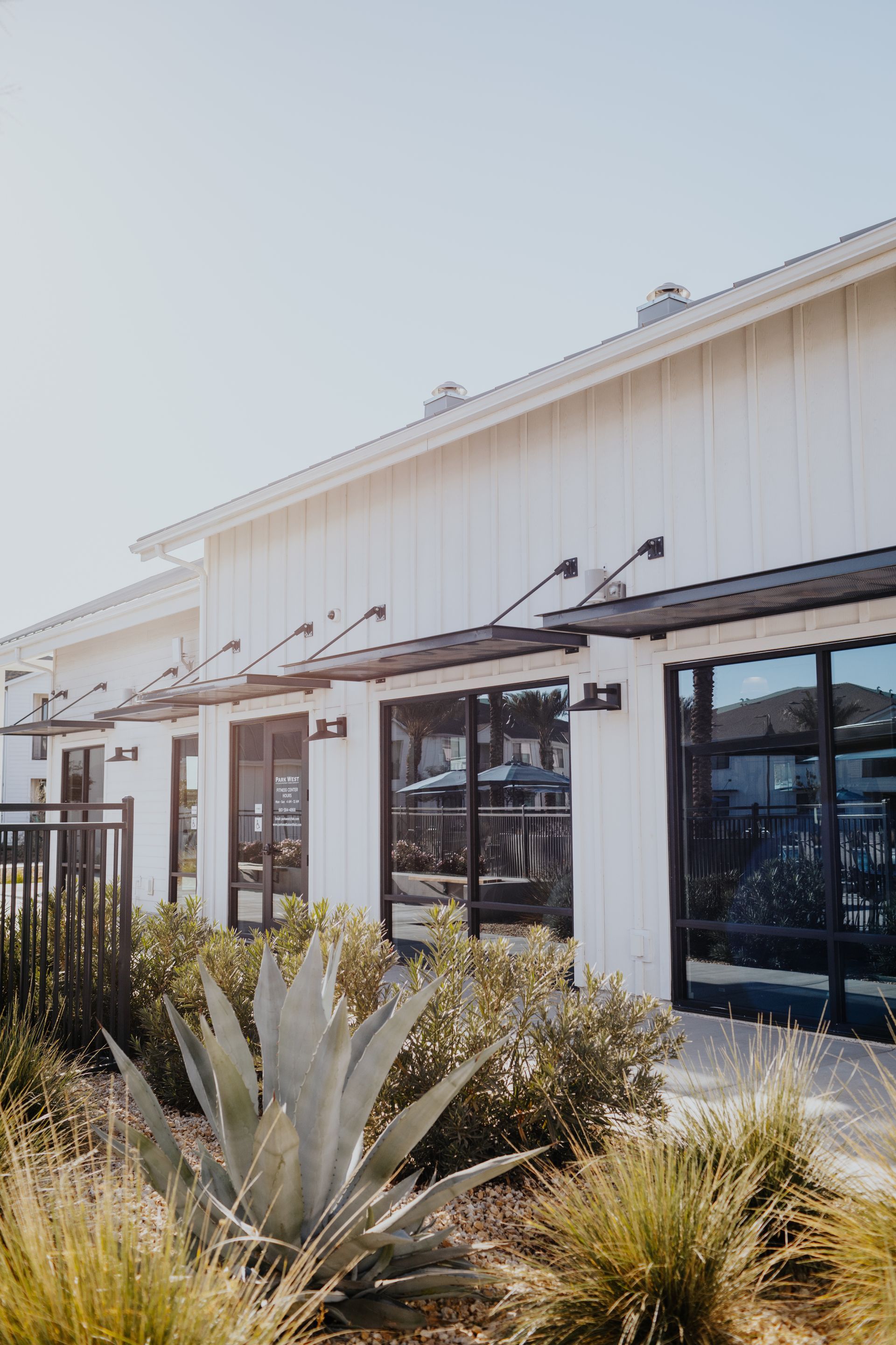 A white building with a lot of windows and plants in front of it.