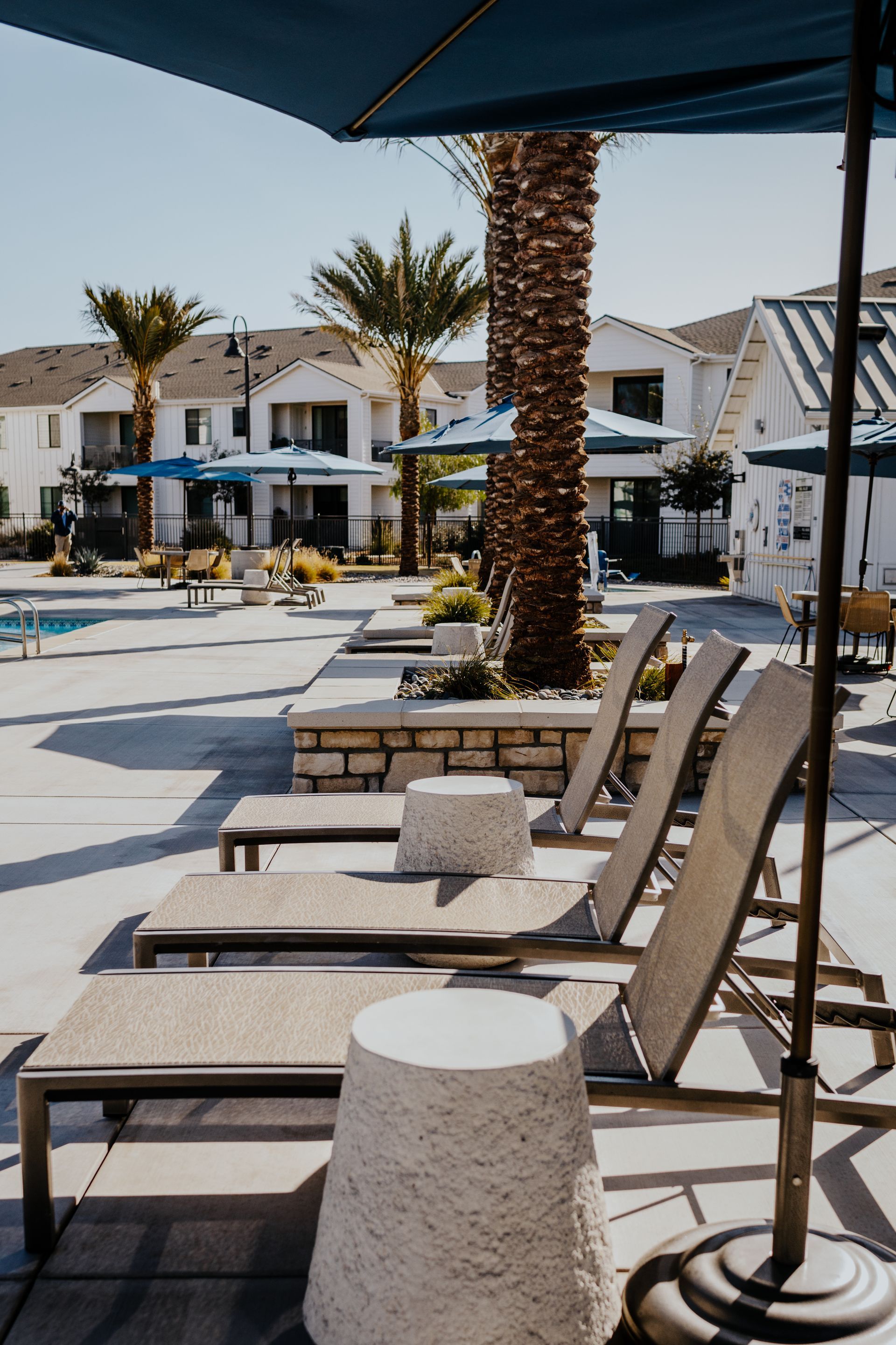 A row of lounge chairs under an umbrella next to a pool.