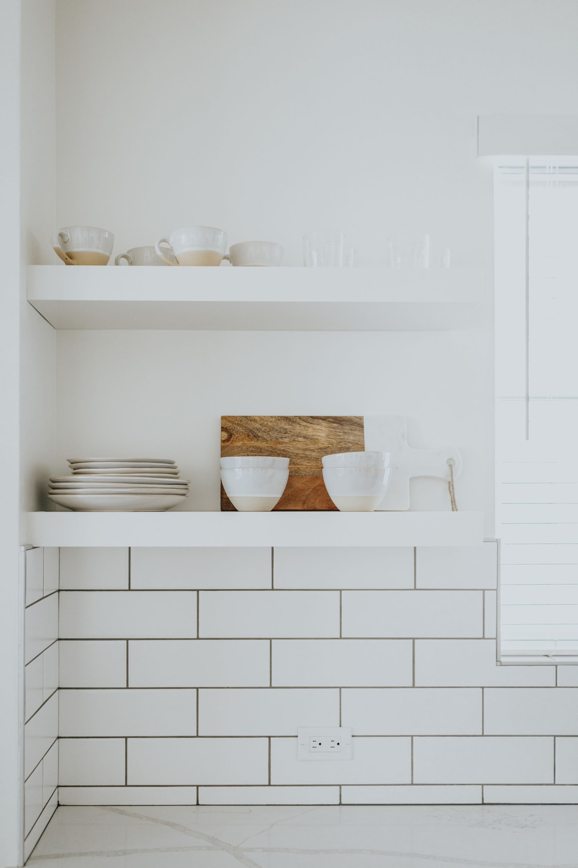 A kitchen with white tiles and shelves filled with bowls and plates.