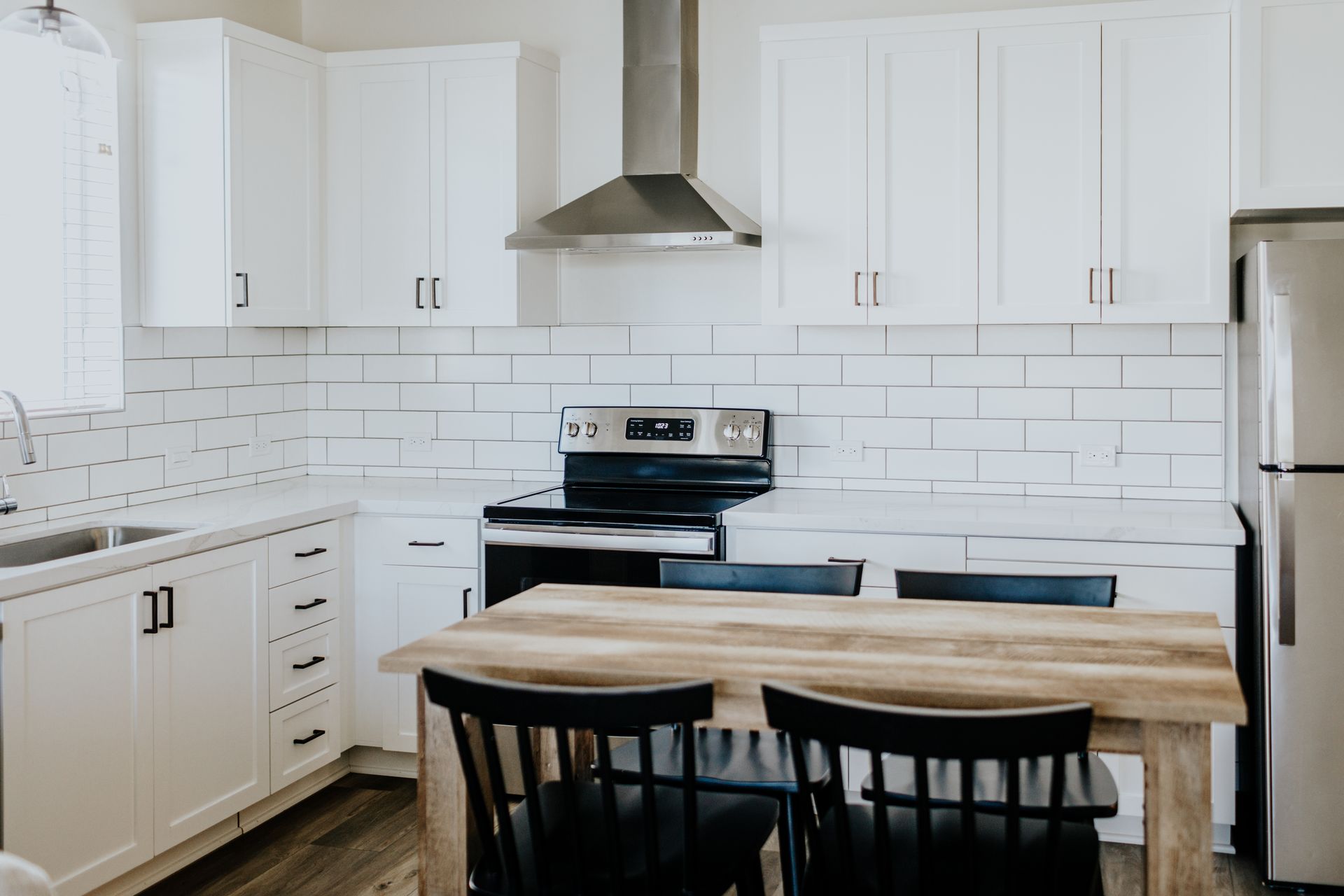 A kitchen with white cabinets , a stove , a refrigerator , a table and chairs.