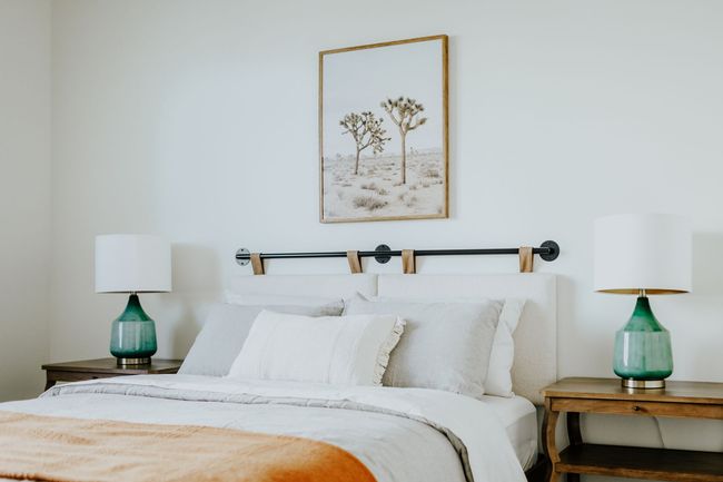 A bedroom with a bed , two lamps and a picture on the wall above the bed.