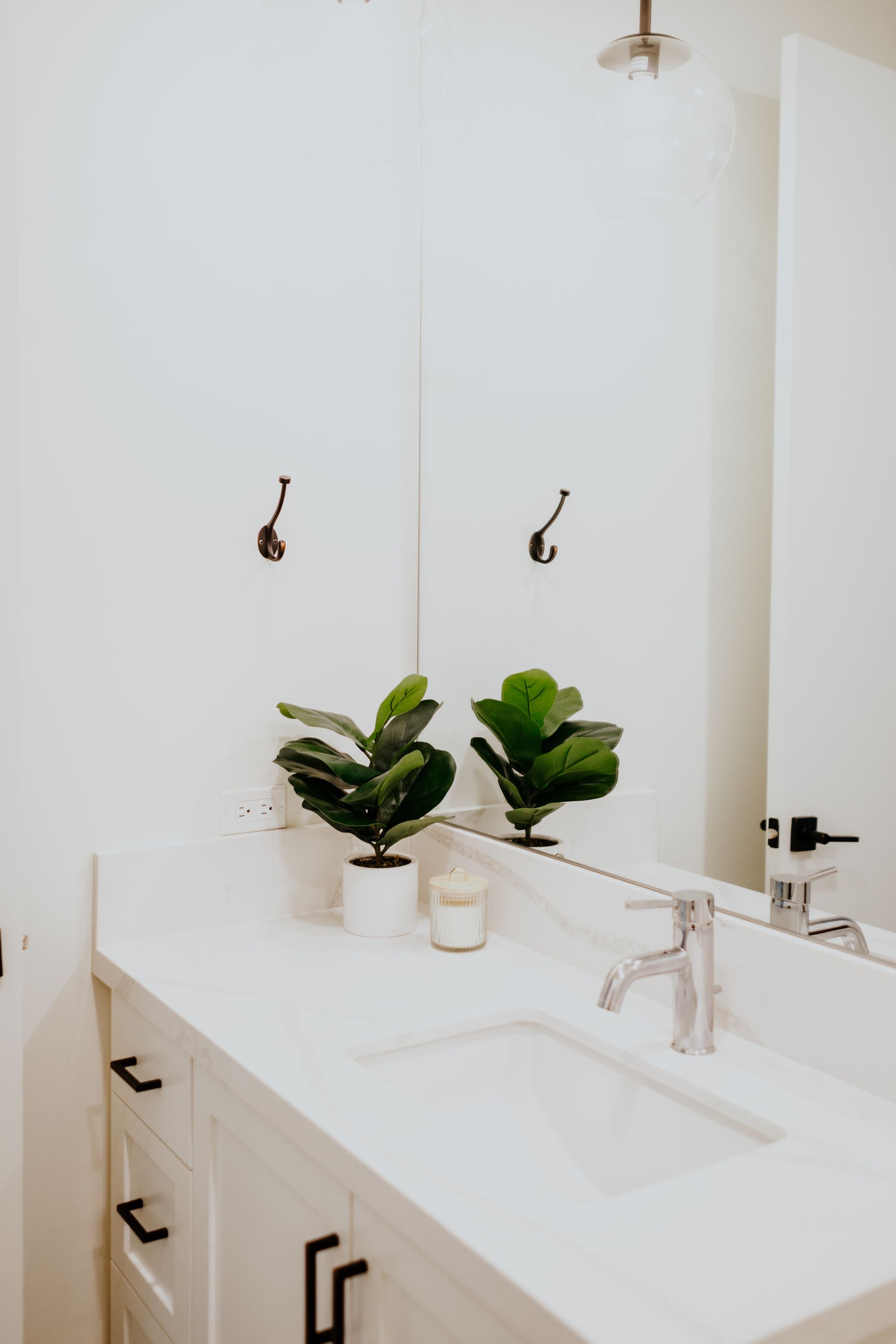 A bathroom with a sink , mirror and two potted plants.