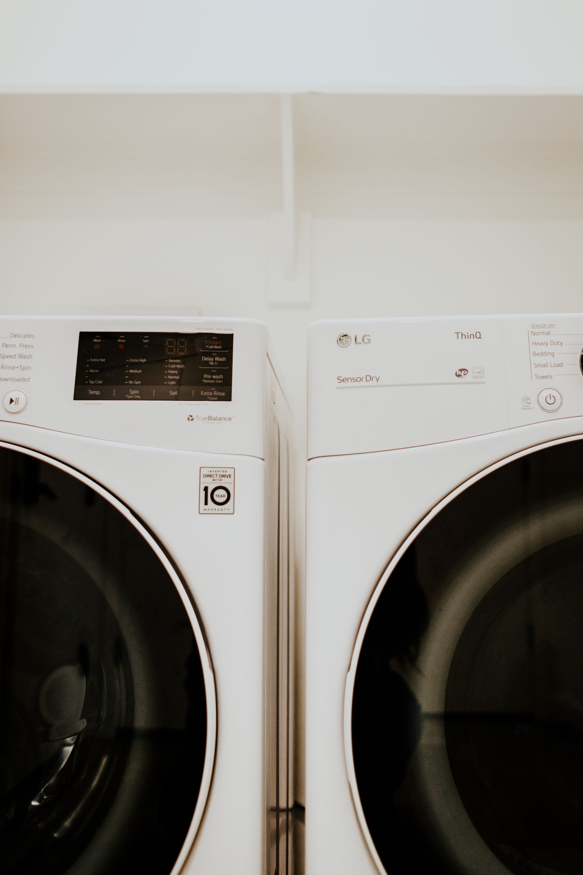 Two white washing machines are sitting next to each other in a laundry room.