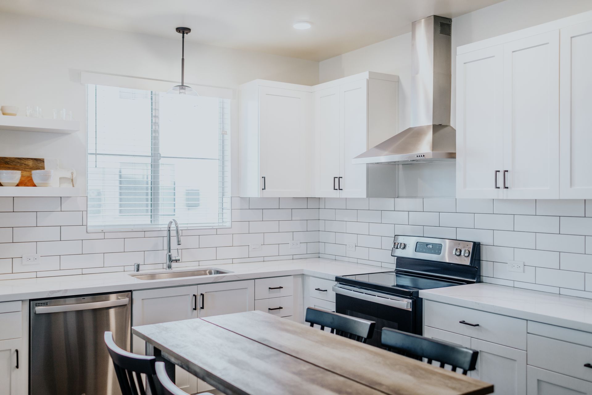 A kitchen with white cabinets , stainless steel appliances , a table and chairs.