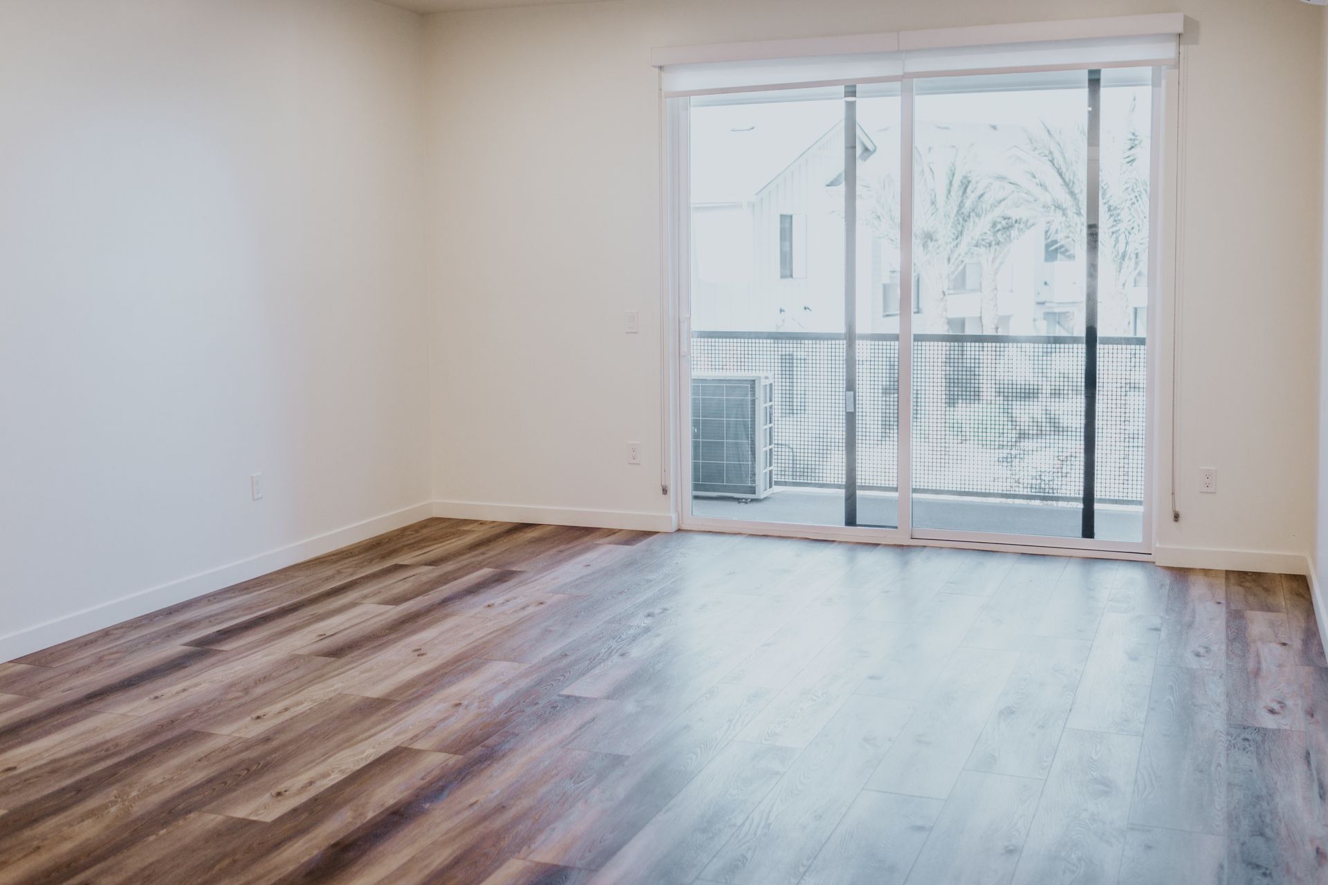 An empty living room with hardwood floors and sliding glass doors leading to a balcony.