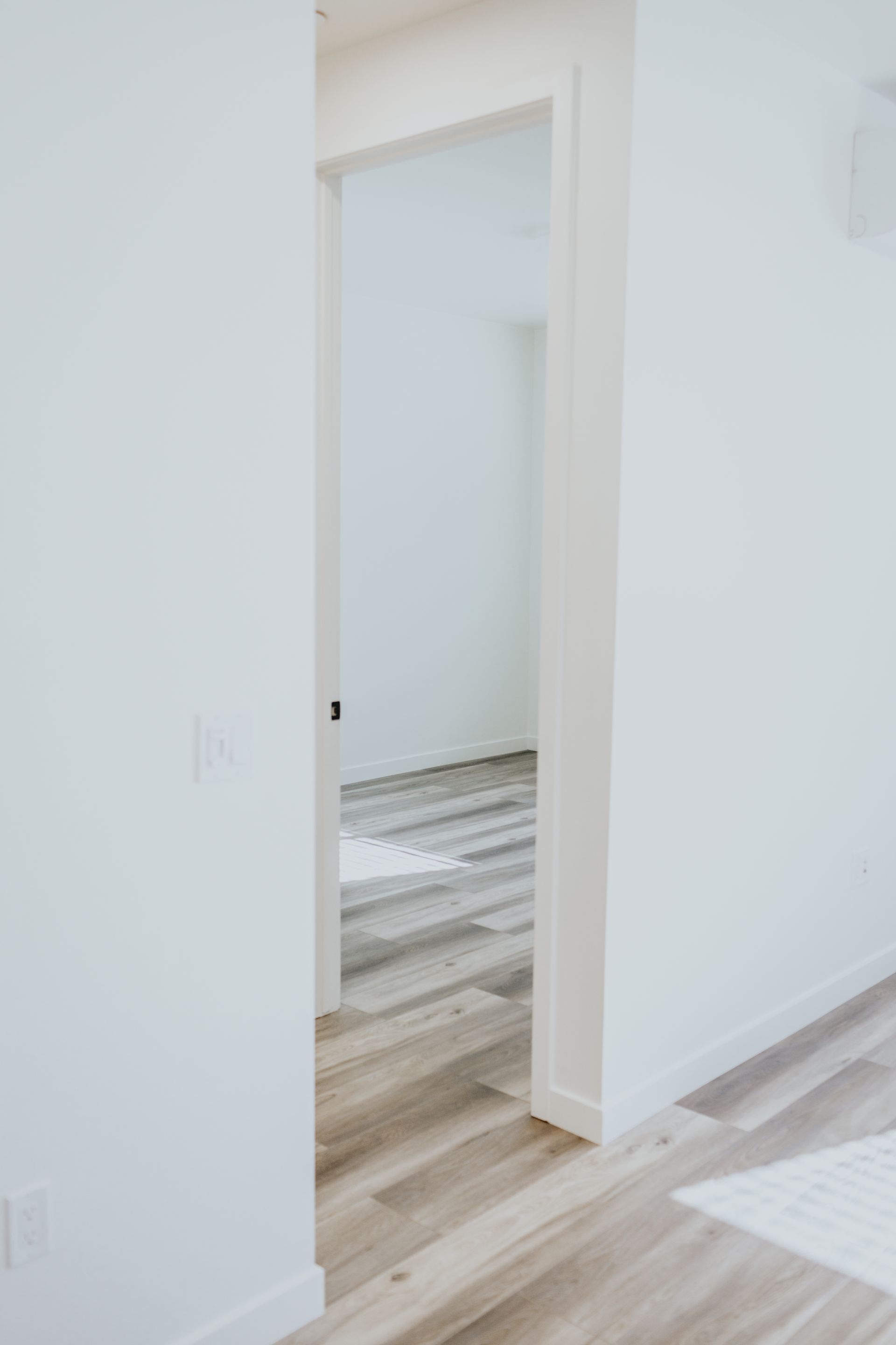 A hallway with white walls and wooden floors leading to an empty room.