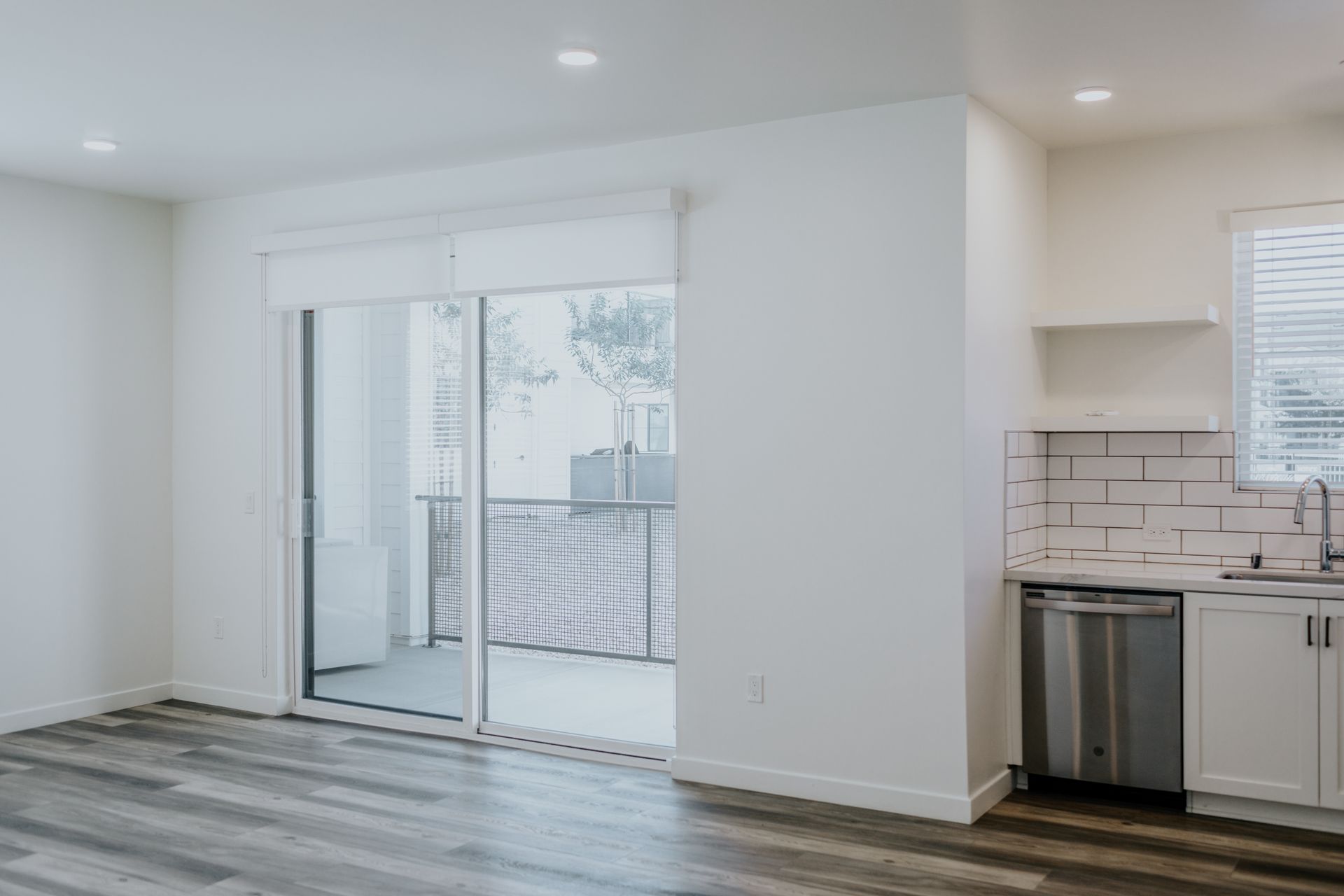 A living room with a sliding glass door leading to a balcony and a kitchen.