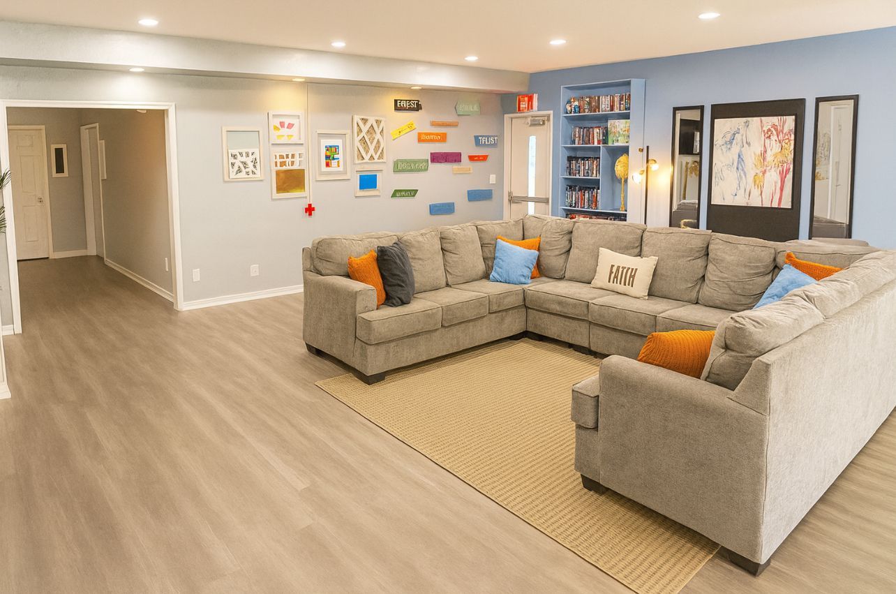 Lounge with gray sectional sofa, art on light blue walls, a rug, and bookshelf.