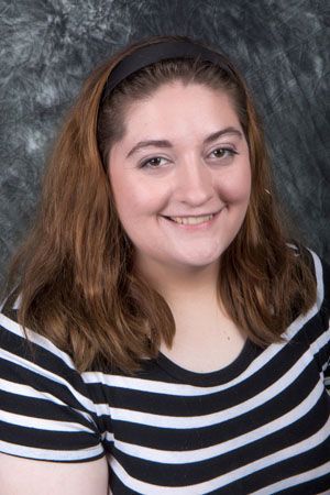 Woman with brown hair smiling, wearing a black and white striped shirt and a black headband.