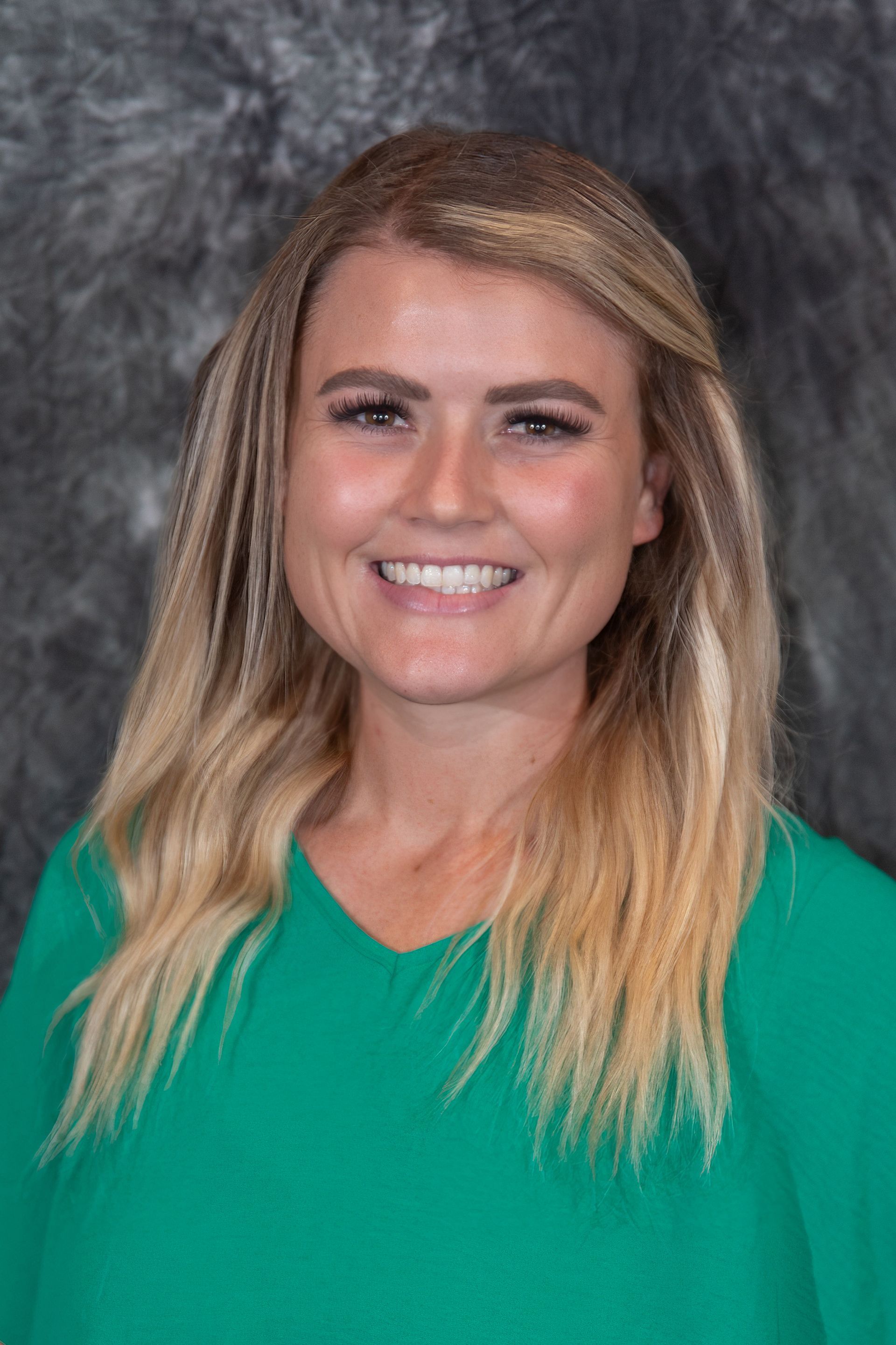 Woman with blonde hair, wearing a black blazer and patterned shirt, smiling at the camera.