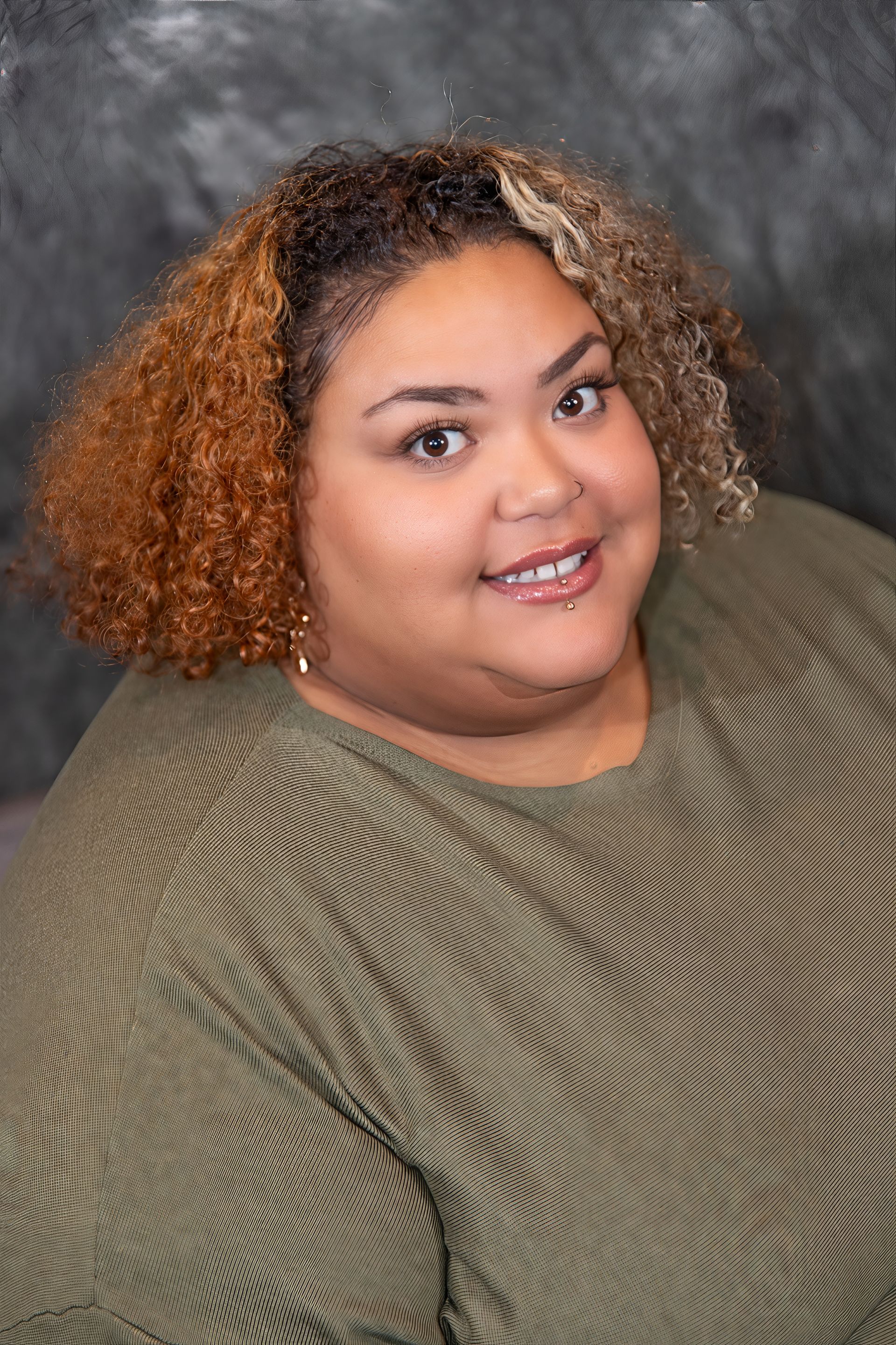 Woman smiling, wearing glasses and a floral yellow jacket over a black top, against a mottled gray backdrop.
