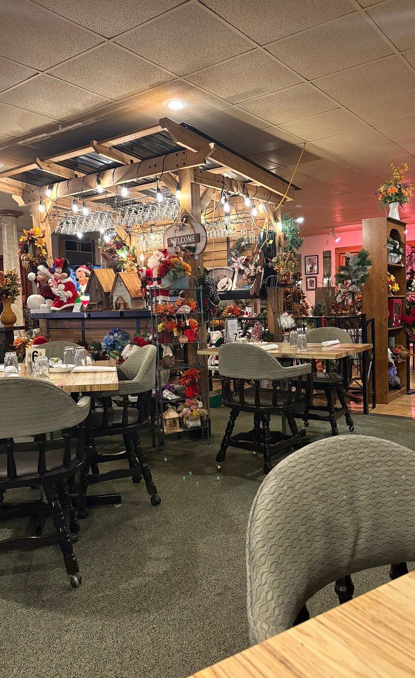 Restaurant interior with tables, chairs, and decorations. A decorative bar area is in the background. Dim lighting.