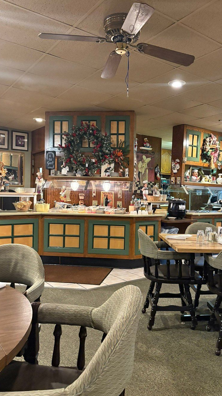 Interior of a diner with wooden booths, tables, and a ceiling fan. A wreath is on a counter.