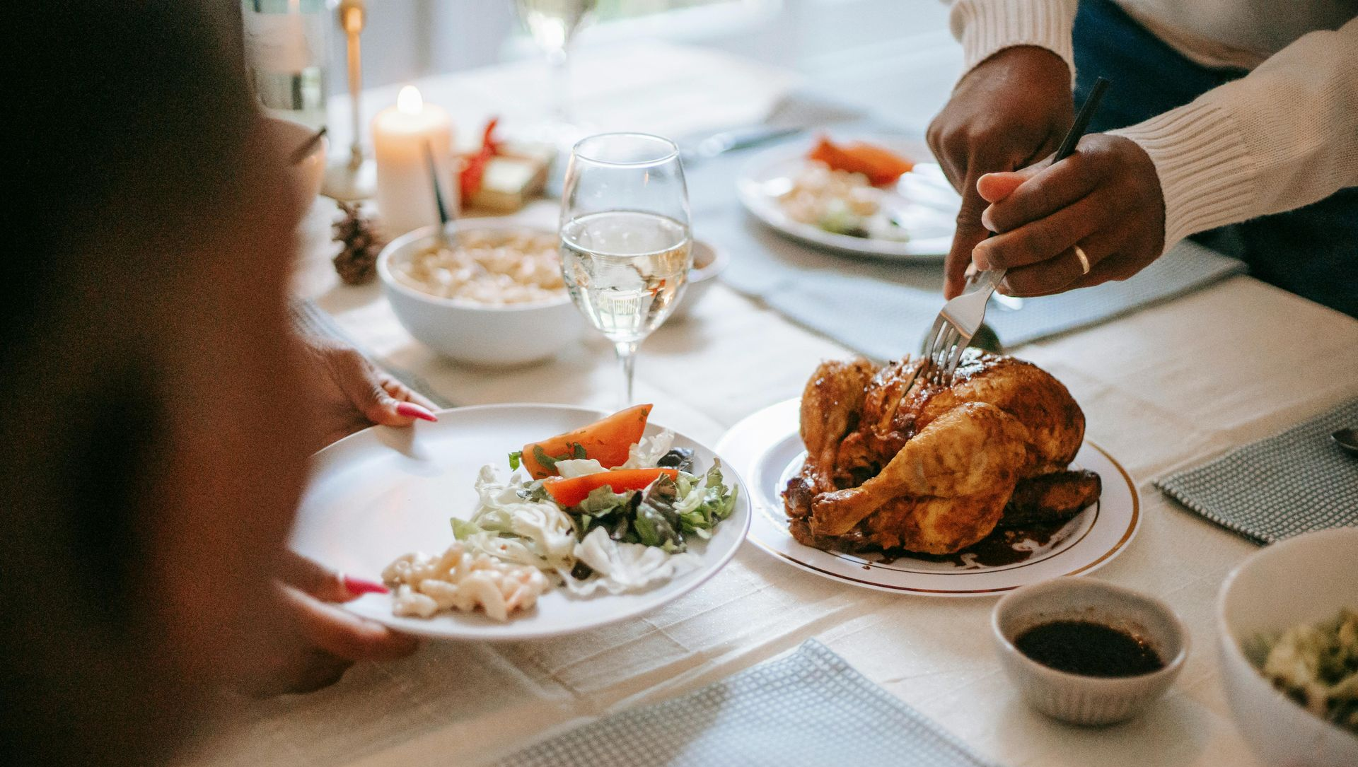 Person carving roasted chicken at a table set for a meal; salad, rice, and drinks are present.
