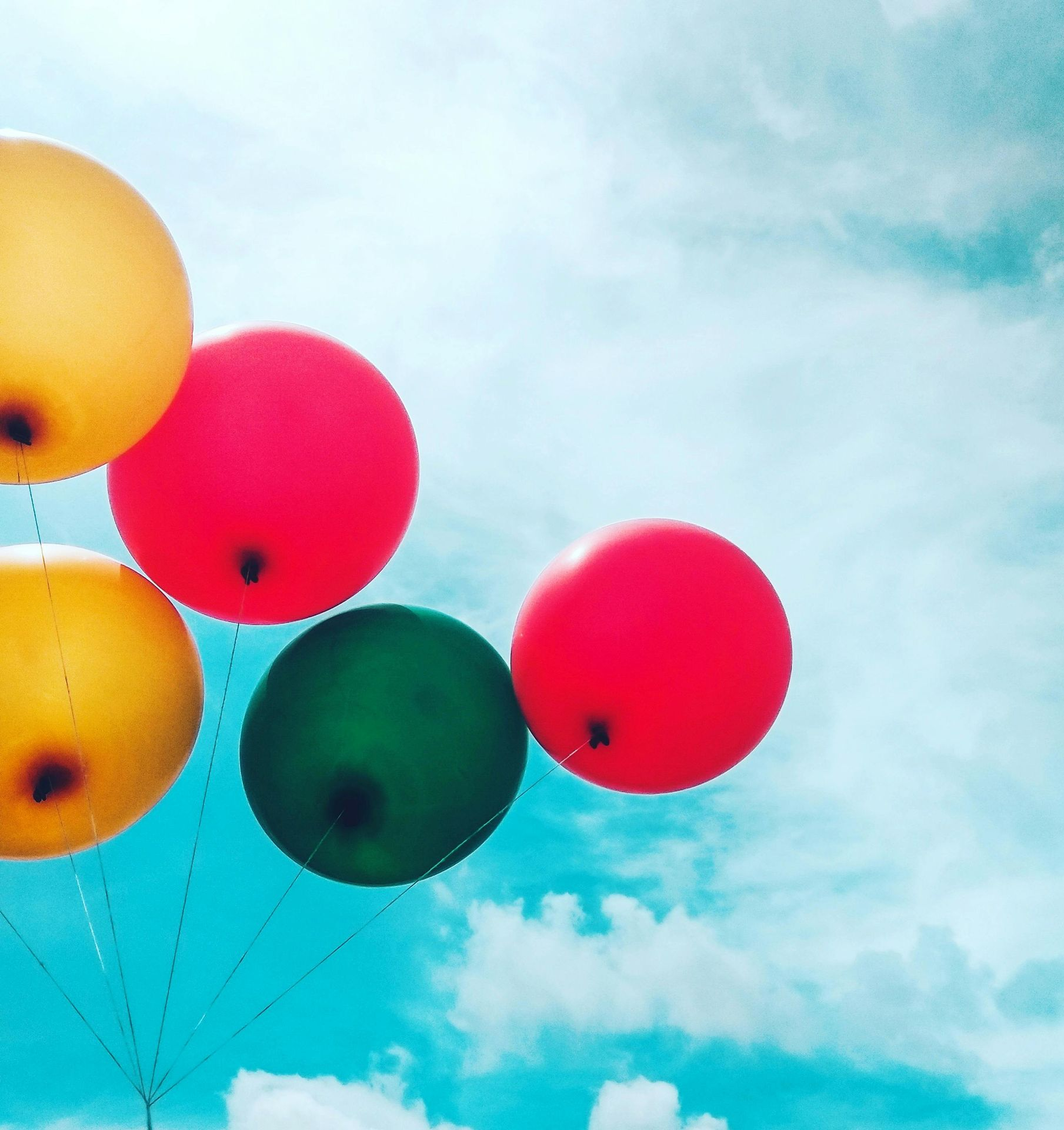 Colorful balloons floating against a bright, cloudy blue sky.