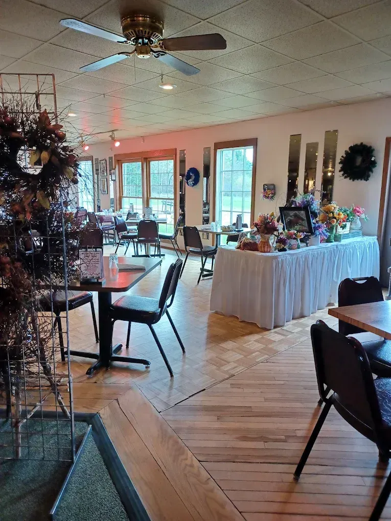 Restaurant interior with tables, chairs, and decorations. Light wood floors, white tablecloth, and large windows.