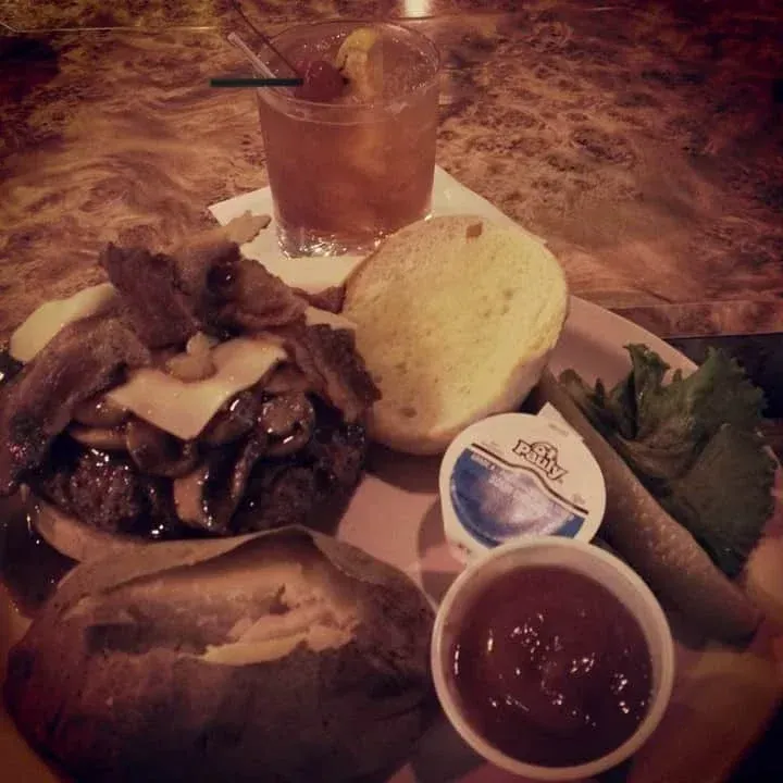 Burger with baked potato, cocktail, and condiments on a plate.