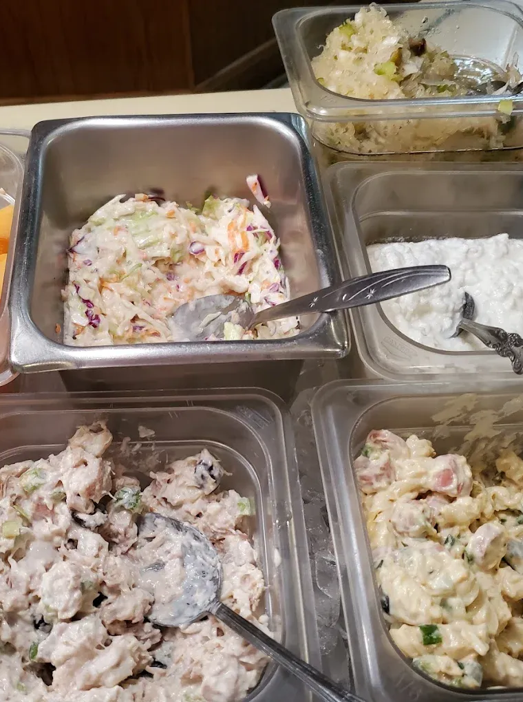 Salad bar with various cold dishes, including coleslaw, chicken salad, and potato salad.