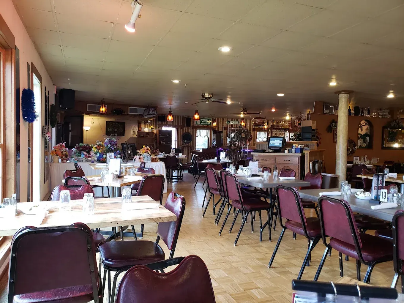 Interior of a restaurant with tables, chairs, and decorations; natural light from windows.