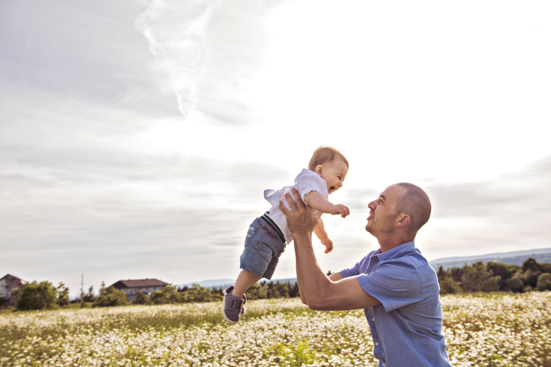 Father lifting and smiling at his young child outdoors, showing a positive parent-child relationship