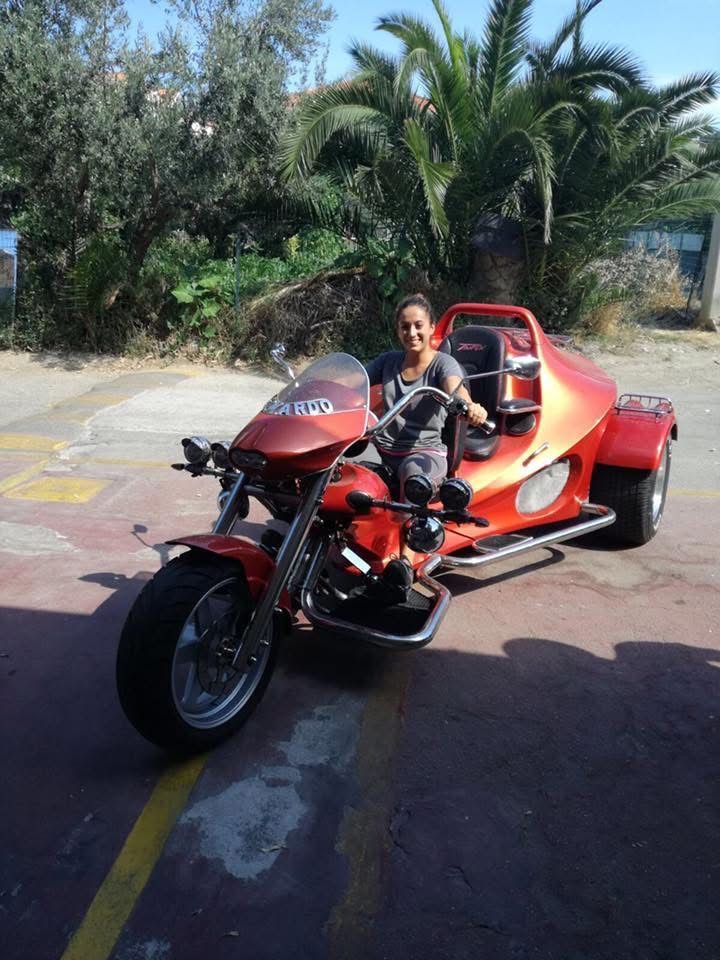 Donna seduta su una motocicletta triciclo rossa con una palma sullo sfondo.