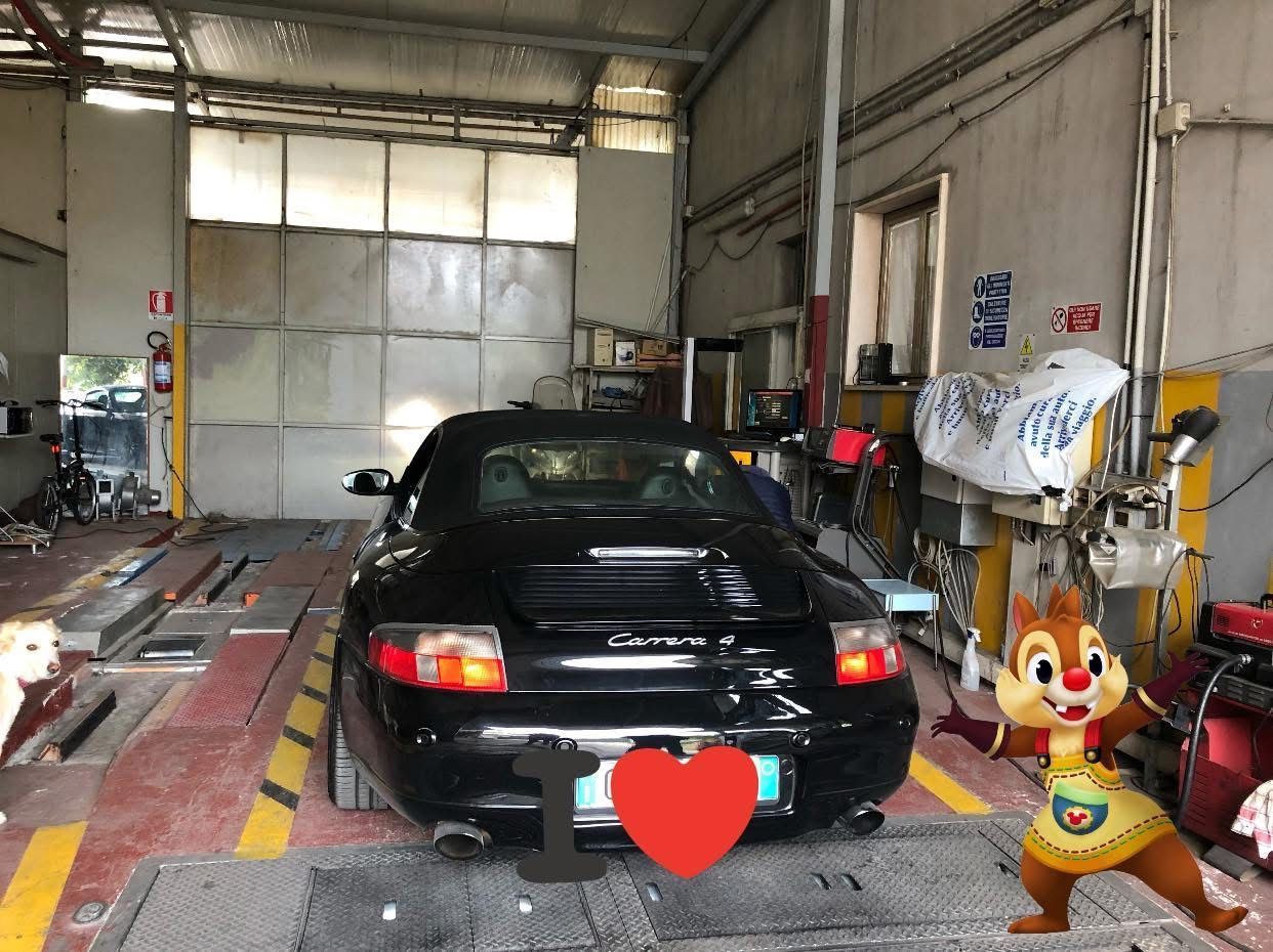 Porsche decappottabile nera in un garage; uno scoiattolo dei cartoni animati tiene un cartello con la scritta 