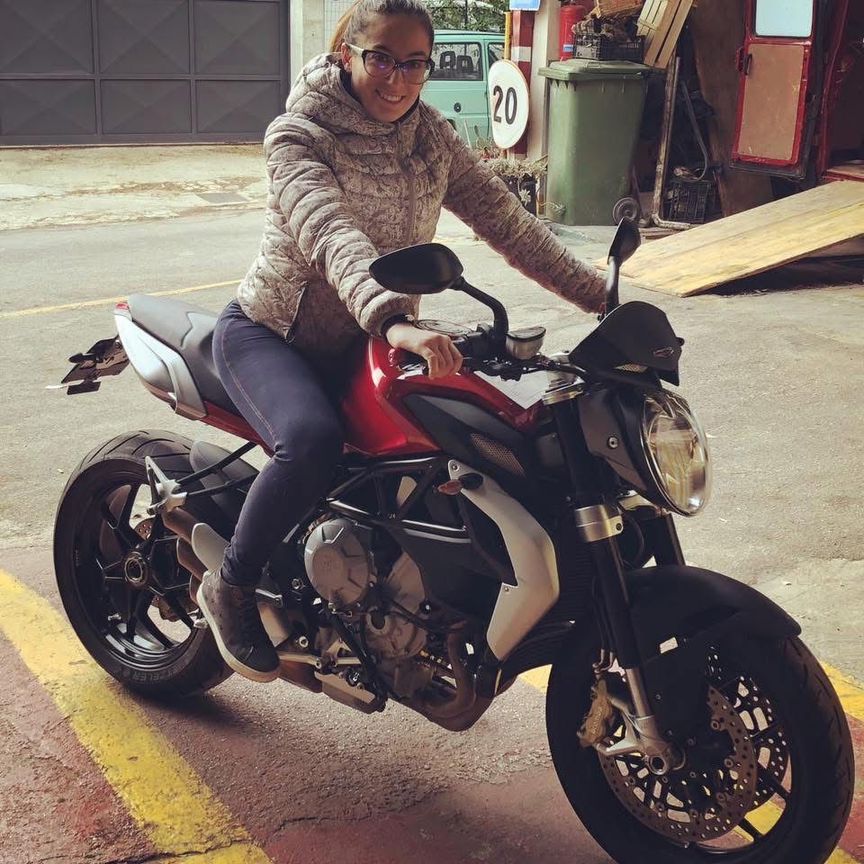 Donna sorridente su una motocicletta rossa e nera, all'aperto.