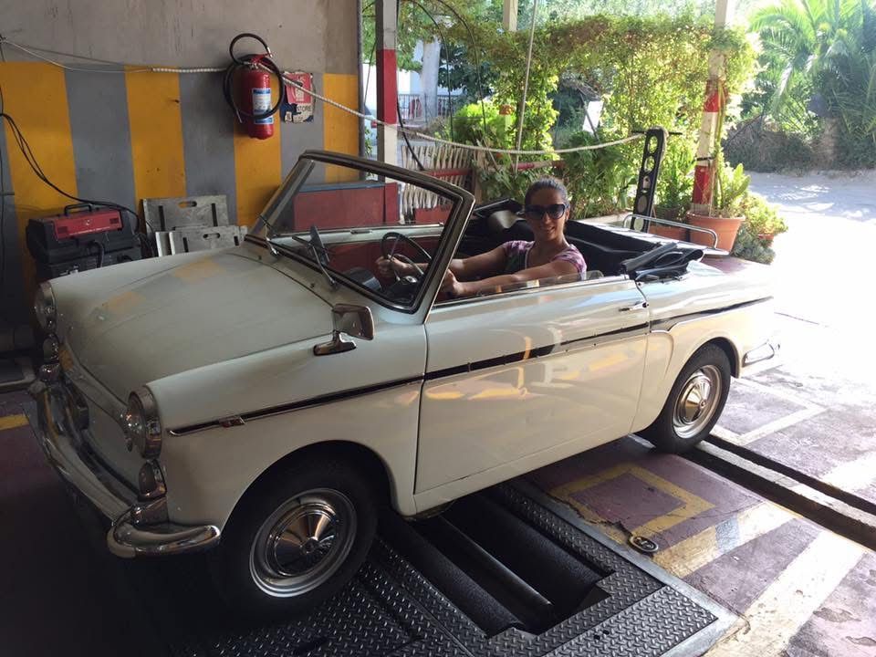 Una persona alla guida di una decappottabile bianca classica in un garage; soleggiato.