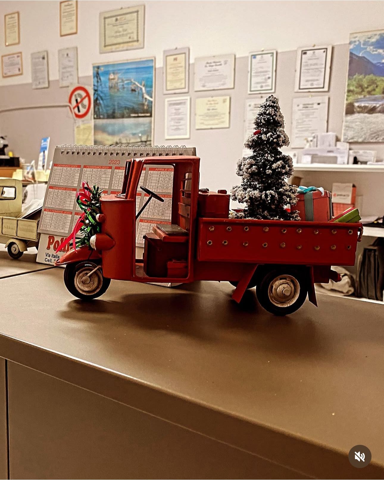 Miniatura di un camion di Natale rosso con albero e regali su una scrivania. Ambiente d'ufficio con documenti.