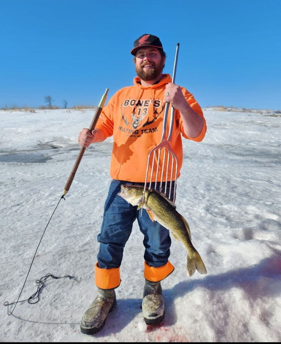 A man in an orange hoodie is holding a fishing rod and a fish