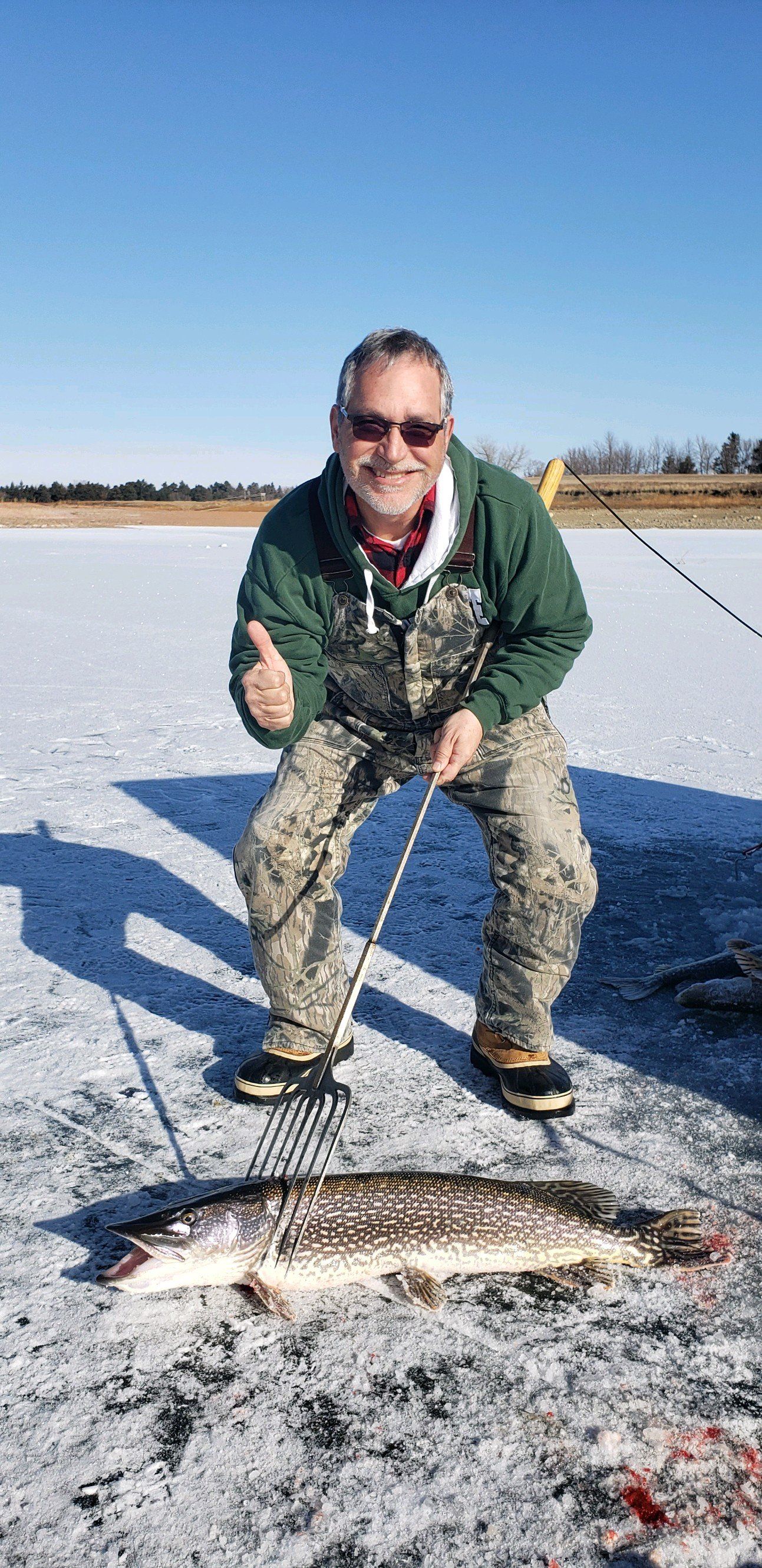 A man is kneeling down next to a large fish on ice.