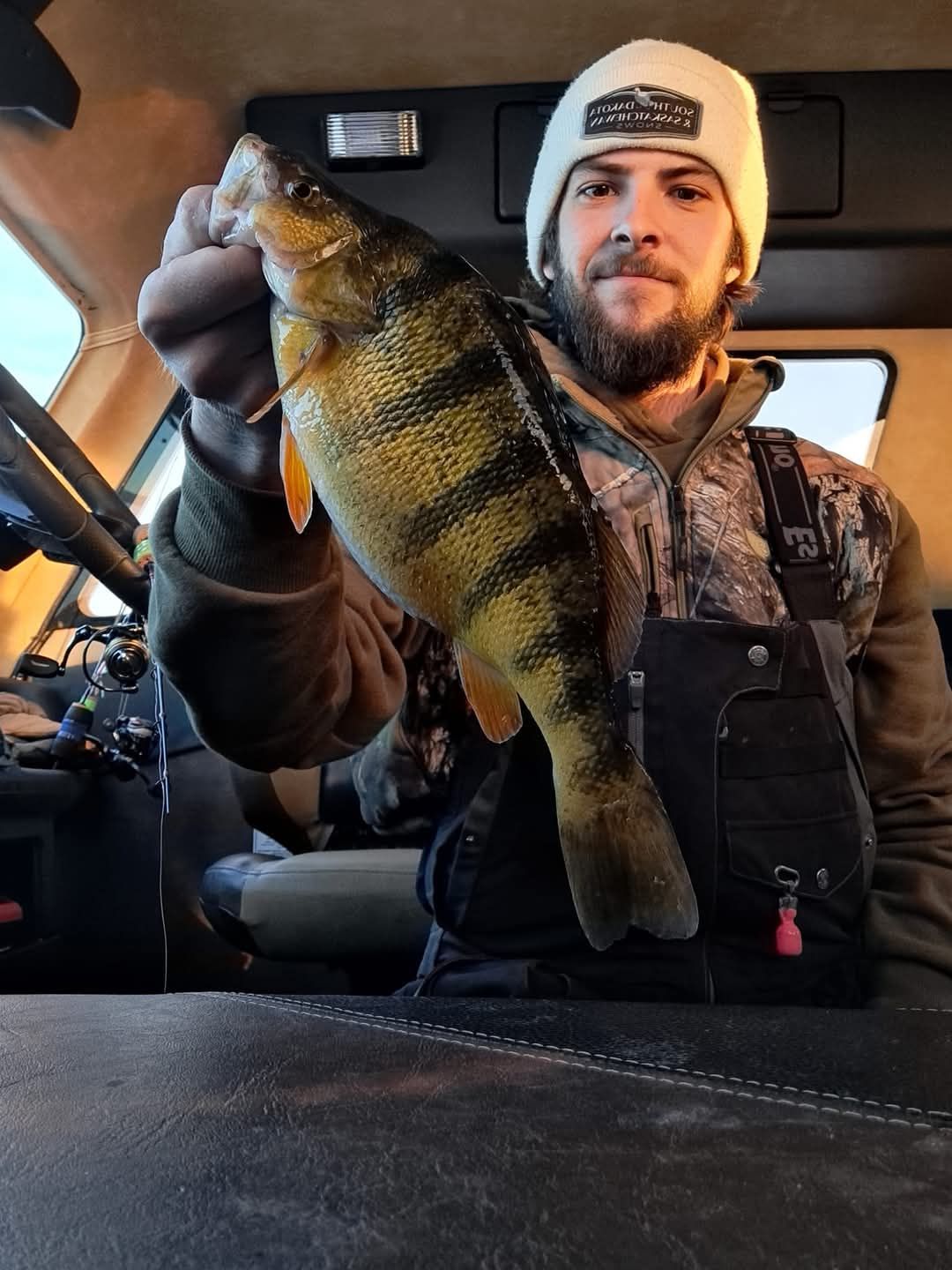 A man is holding a fish in his hand in a car.