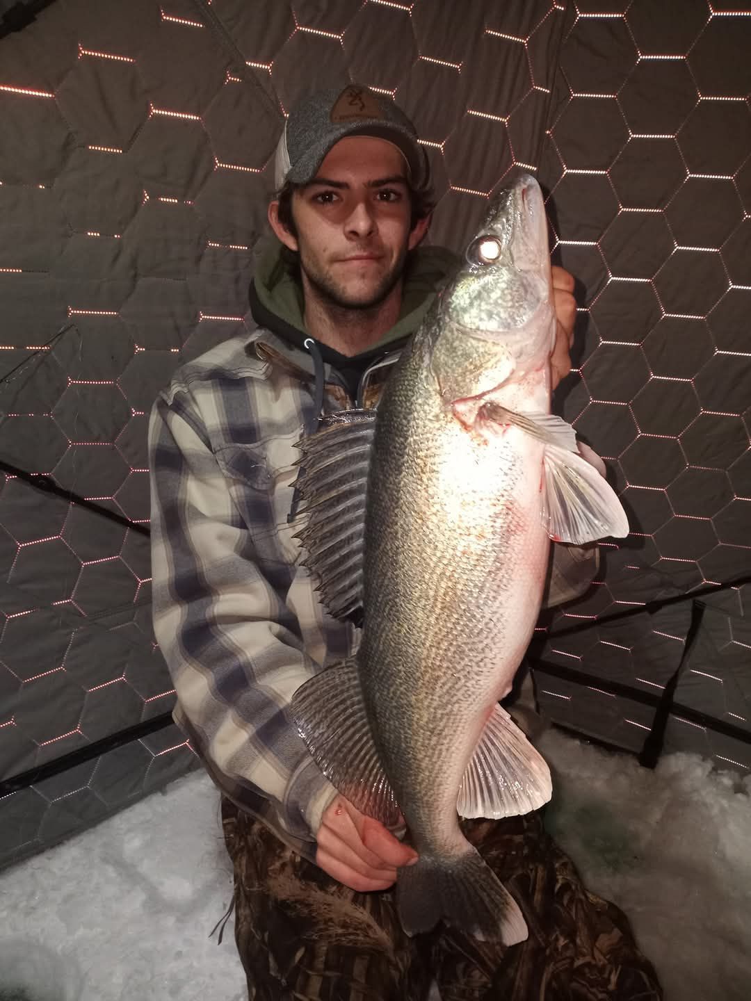 A man in a plaid shirt is holding a large fish