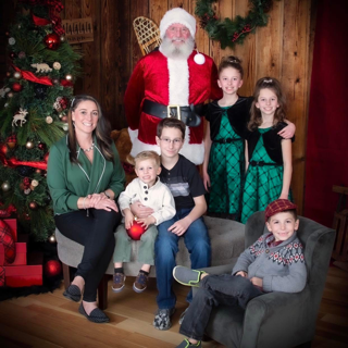 Family with Santa in front of Christmas tree. Mother and children smile. Wooden background.