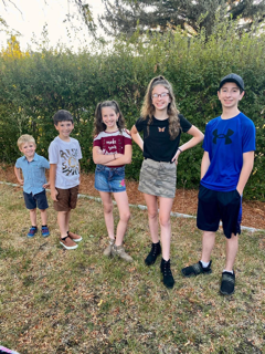 Five children standing outdoors on grass, posing.