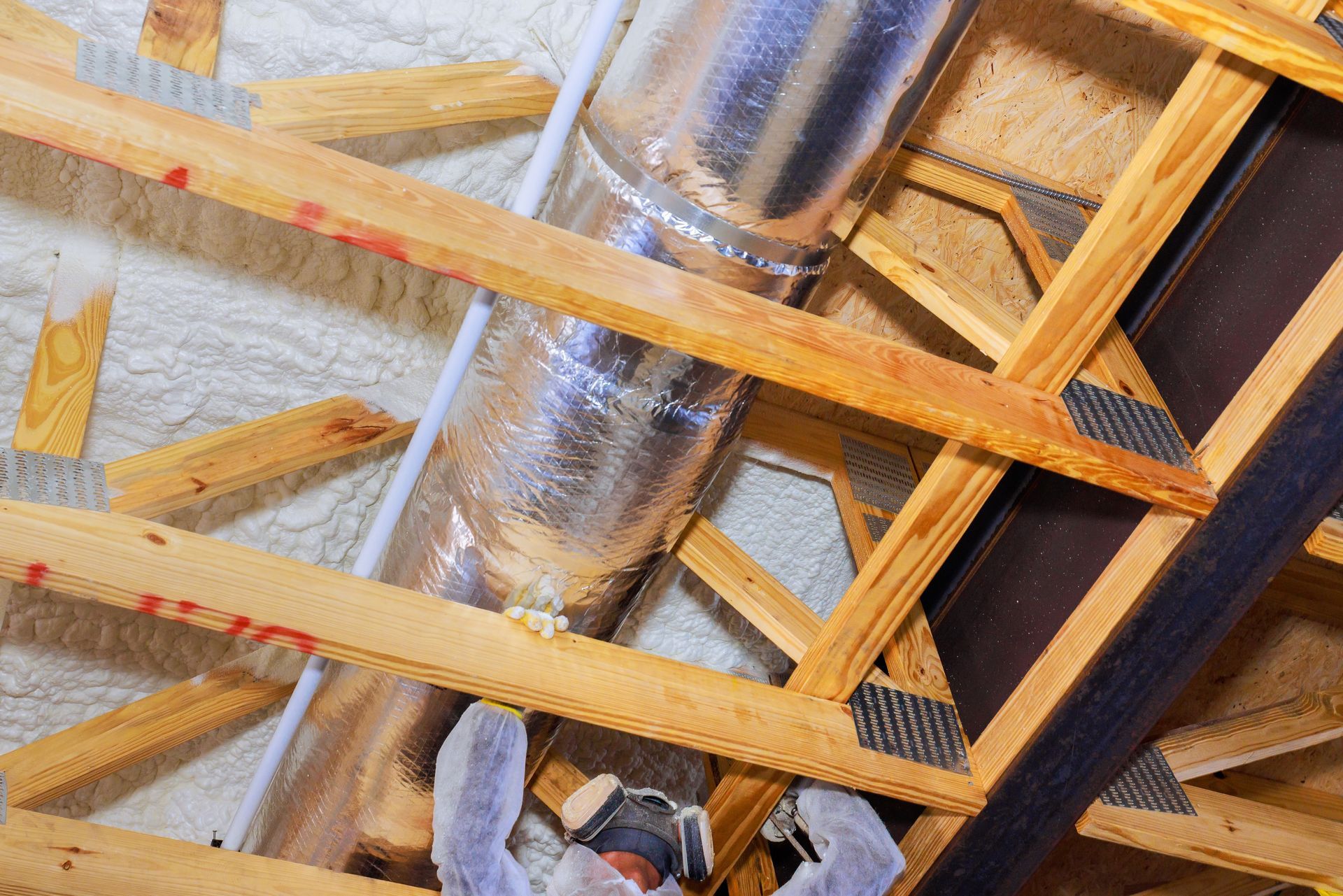 Person installing ductwork in attic with insulation, wooden beams and trusses.