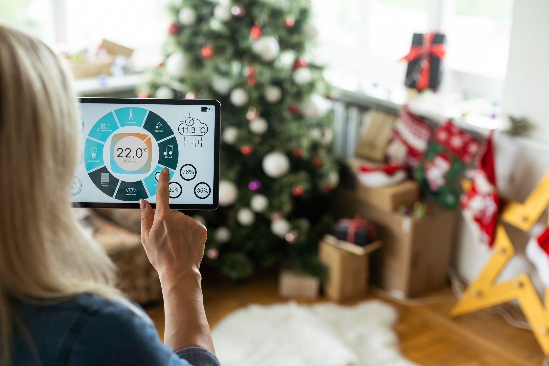 Woman adjusting smart home controls on a tablet in a Christmas-decorated living room.